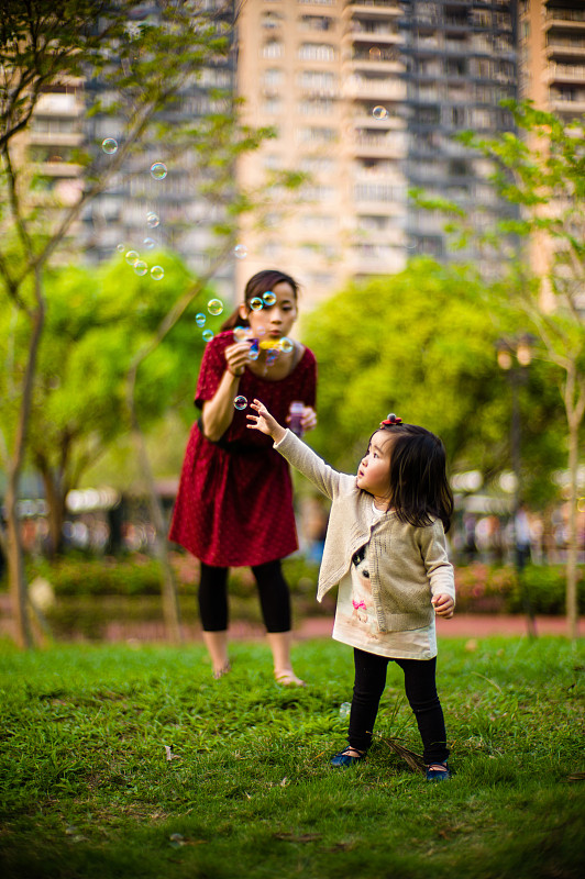 年轻的妈妈和蹒跚学步的孩子玩泡泡棒图片下载