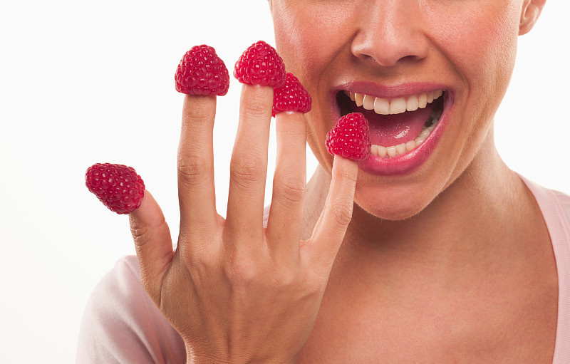 近距离的女人咬树莓的指尖图片素材