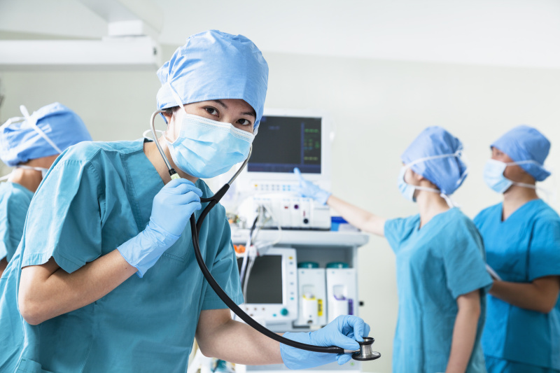 一组外科医生在手术室里，女外科医生拿着听诊器看着摄像机图片下载