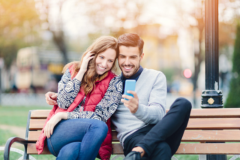 一对年轻夫妇正在公园里休息，用着智能手机图片下载