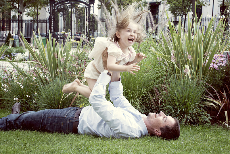父亲躺在草地上，开玩笑地把小女儿举到空中图片下载