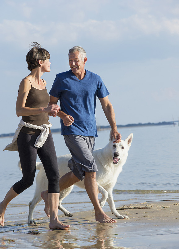 一对白人夫妇和狗在海滩上慢跑图片下载