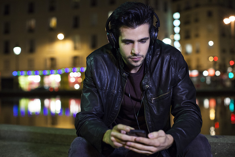 一个年轻人晚上独自坐在户外戴着耳机听音乐图片下载