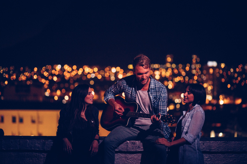 一个年轻人在屋顶上为他的两个朋友弹吉他图片素材