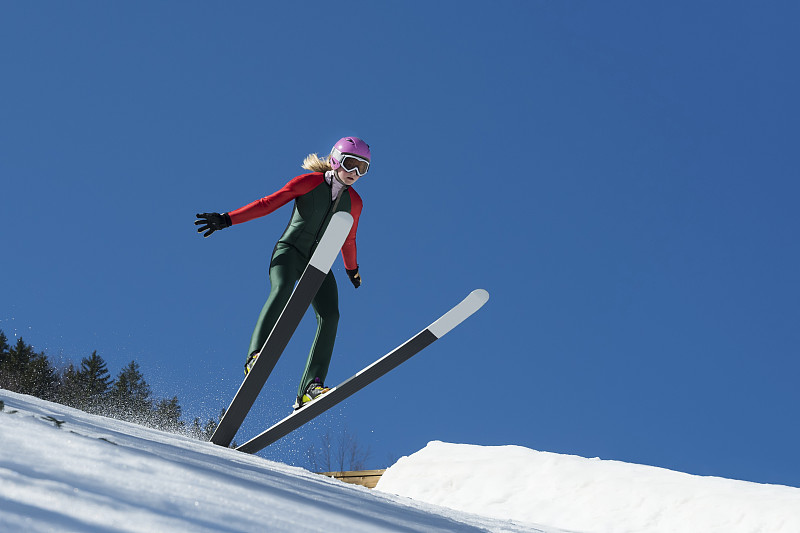 年轻女子跳台滑雪在蓝天下着陆图片下载