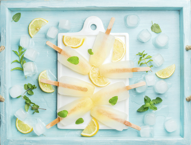 白色的陶瓷板上放着柠檬冰棒，配上柠檬片、冰块和薄荷叶，以蓝绿色为背景图片素材