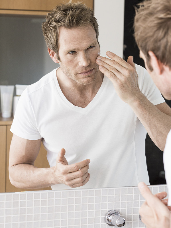 Mid adult man looking in bathroom mirror applying face cream图片下载