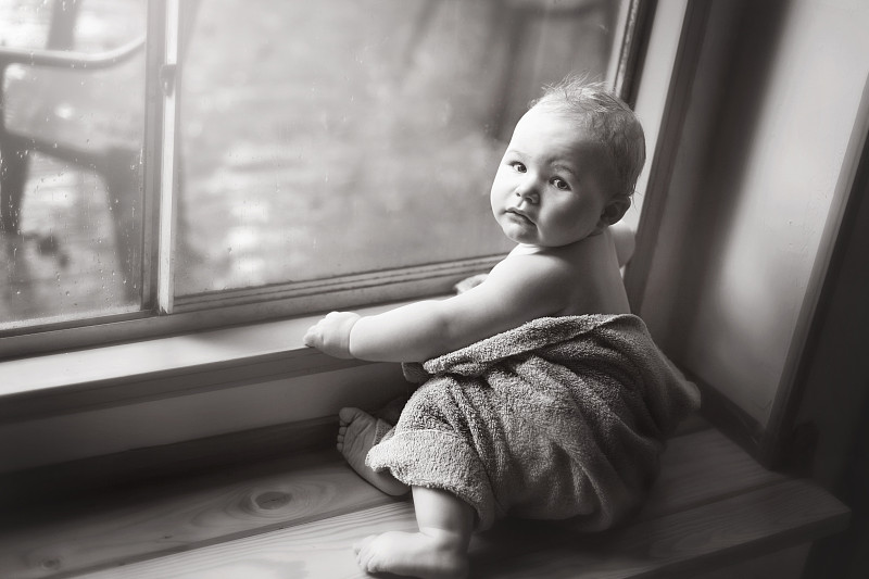 婴儿裹着毛巾坐在靠窗的座位上图片下载