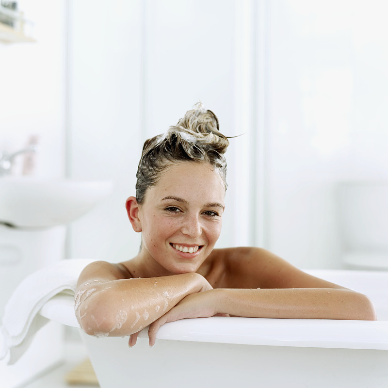 一名年轻女子坐在浴缸里，头发上抹着洗发水的肖像图片下载