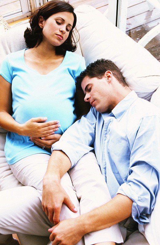 一个孕妇睡在沙发上，腿搁在她丈夫身上的高角度视图图片下载