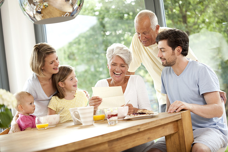 快乐的孙女和她的家人在早餐桌上读信图片下载