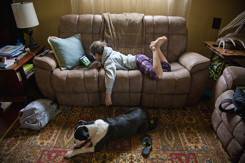10岁的男孩穿着睡衣躺在沙发上，手里拿着平板电脑图片素材