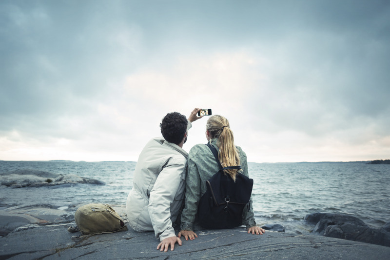 一对情侣坐在海边的岩石上自拍图片下载