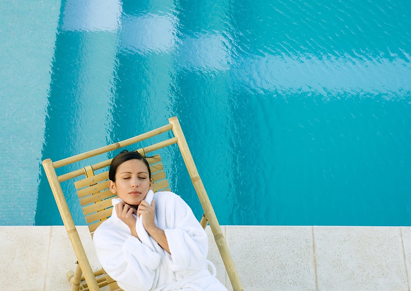 女人躺在泳池边的躺椅上，穿着浴袍图片下载