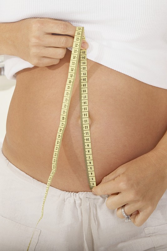 一个孕妇用卷尺测量她的腹部的中段视图图片下载