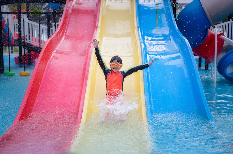 亚洲小孩小男孩玩和有乐趣滑滑梯在水上公园图片素材