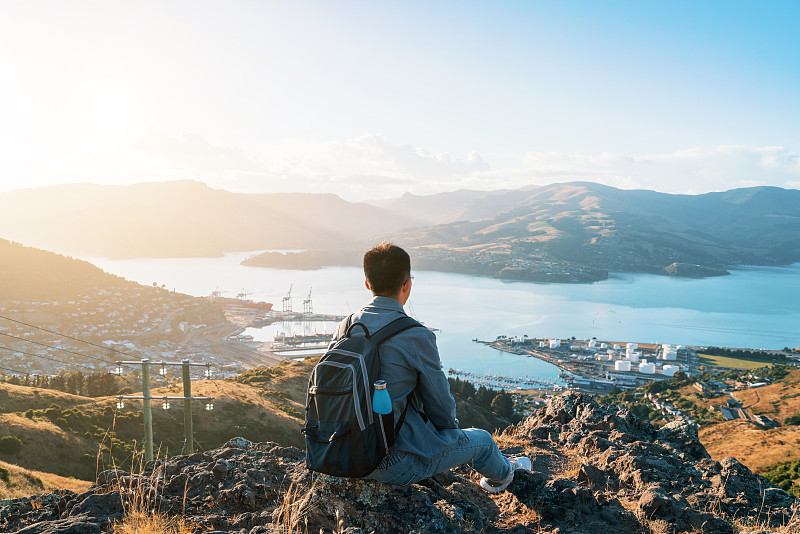 一位年轻的亚洲男子在新西兰的山顶上欣赏美丽的自然景观图片下载