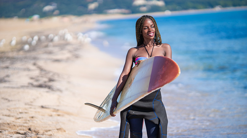 非洲妇女拿着冲浪板在海滩上行走图片素材