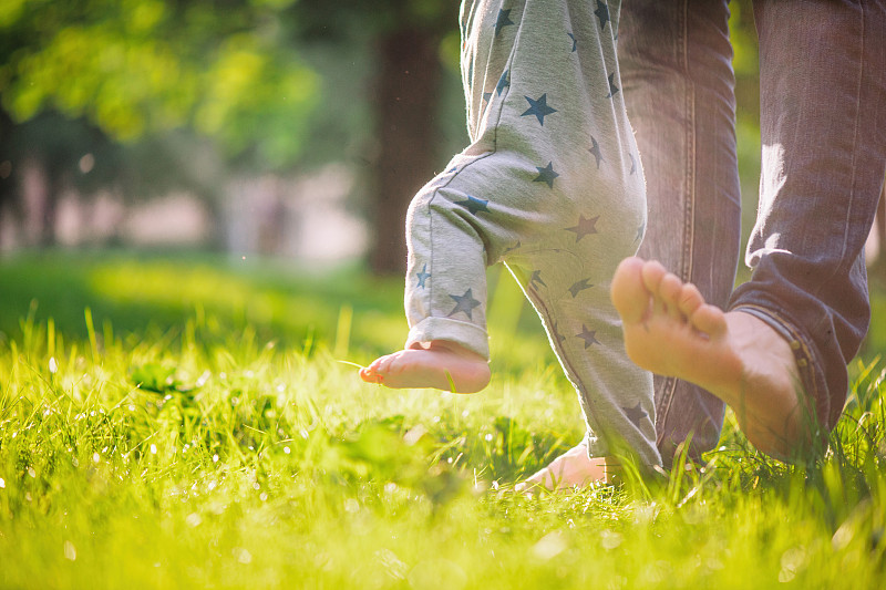 在夏天的草地上，小男孩很高兴他的父亲扶着他迈出了第一步图片下载