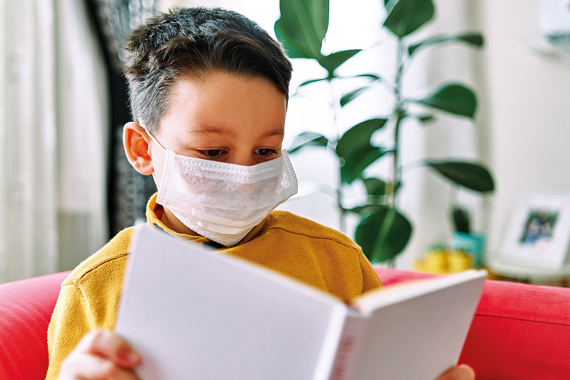 6-7岁可爱的孩子戴着外科口罩在家看书。图片下载