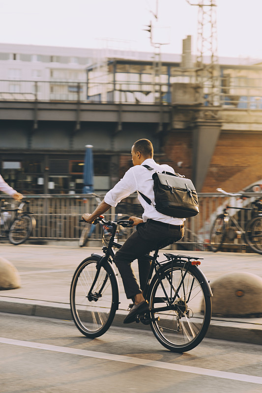 罕见的男性行政人员骑着自行车在城市街道上对着天空图片下载