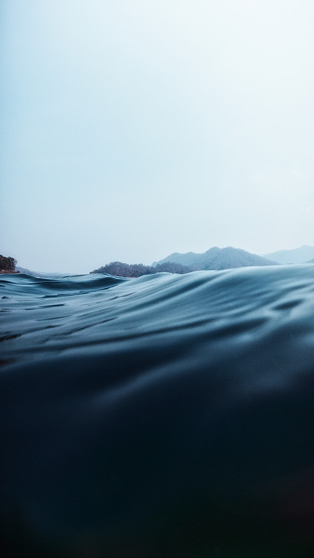 在湖岸边有山的深蓝色海水中，湖表面上下分开的一层图片下载