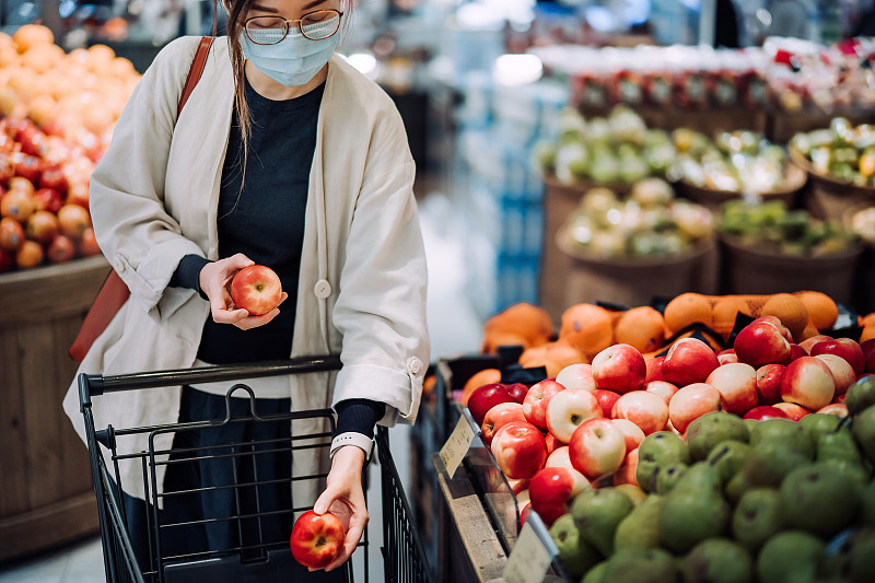 2019冠状病毒病健康危机爆发期间，年轻的亚洲女性戴着防护口罩在超市购买新鲜食品图片下载