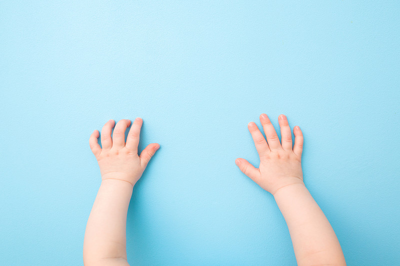 两只婴儿的手放在浅蓝色的桌子背景上。柔和的颜色。特写镜头。视角拍摄。自顶向下的观点。图片素材