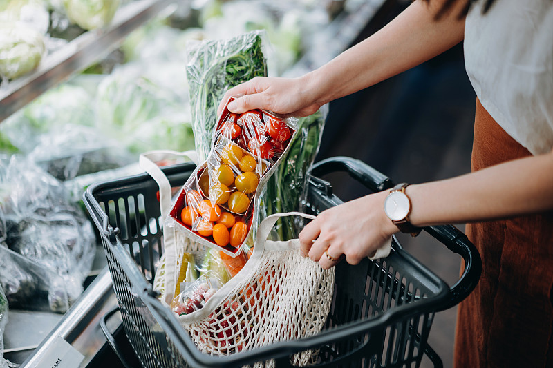 裁剪的镜头年轻的亚洲妇女在超市购买新鲜的有机食品杂货，并把各种水果和蔬菜放入棉花网生态袋在购物车。“零浪费”的概念图片素材