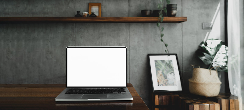 笔记本电脑空白白屏幕上的桌子在咖啡馆的背景。笔记本电脑与空白屏幕上的咖啡店模糊背景。图片素材