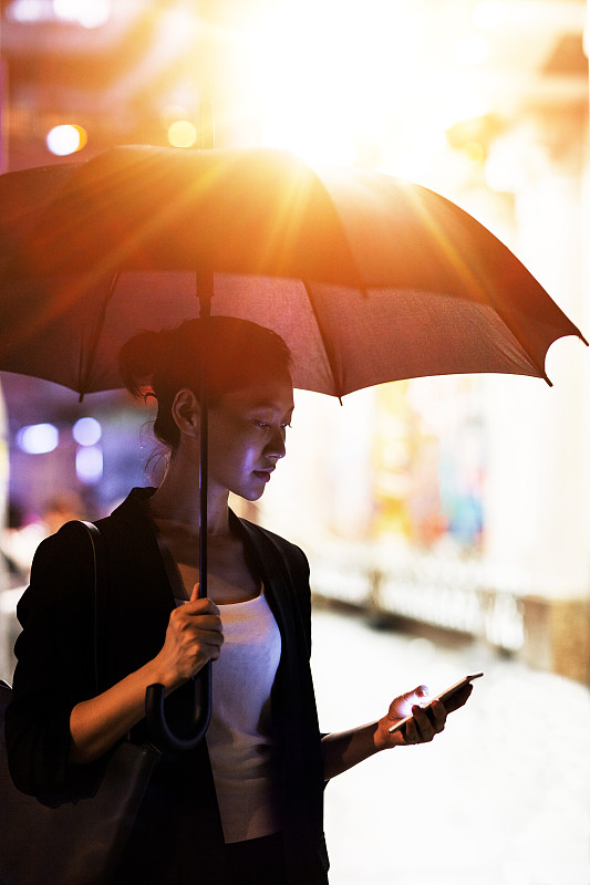 在香港，年轻的中国女商人拿着雨伞拿着手机图片素材