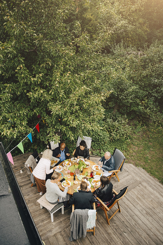 高角度的妇女服务朋友坐在餐桌在花园聚会在后院图片素材