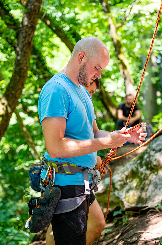 男运动员在户外攀岩时系绳结图片下载