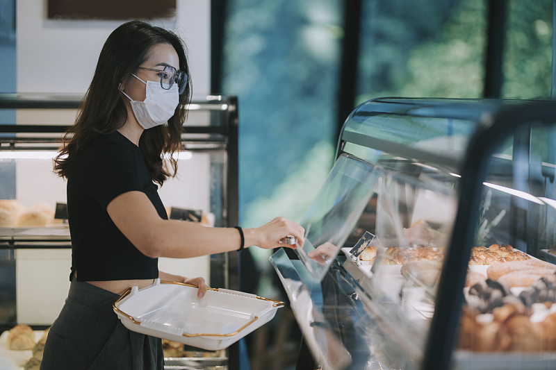 亚洲中国美丽的女人买糕点从一个咖啡馆选择拿着一个托盘图片下载