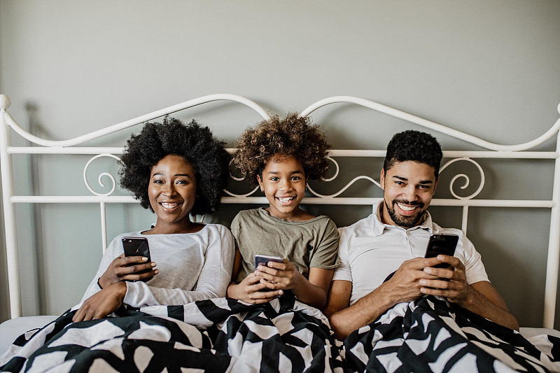 年轻的非洲裔美国家庭在床上使用手机图片下载