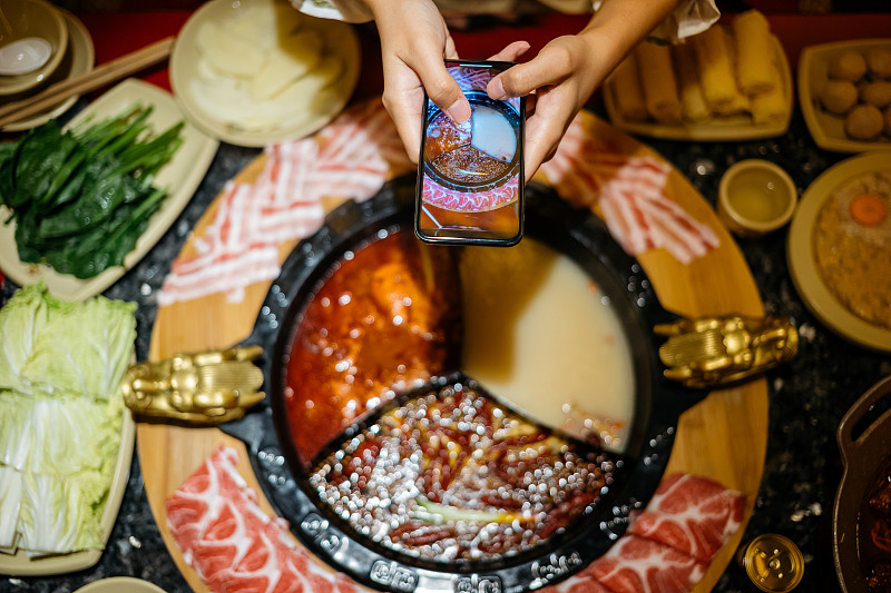 一名亚洲中国女性正在用智能手机拍摄她的火锅晚餐图片下载