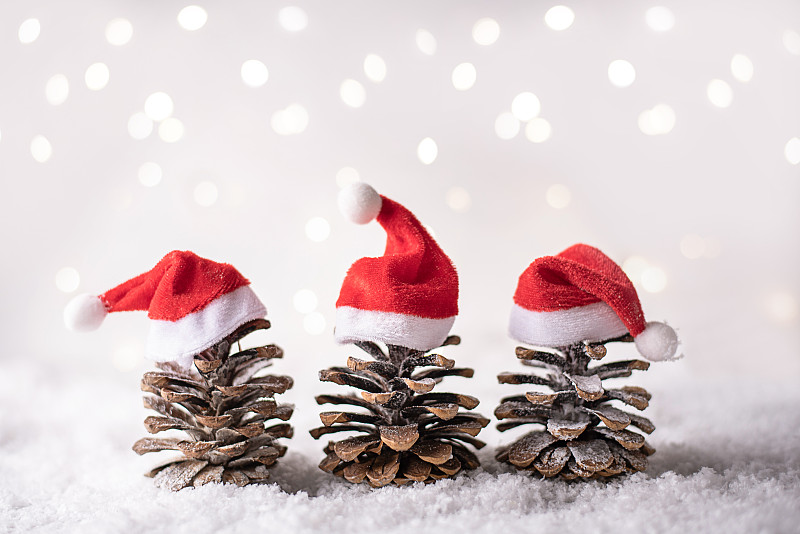 三个松果戴着圣诞帽，像白色背景上的圣诞树。图片下载