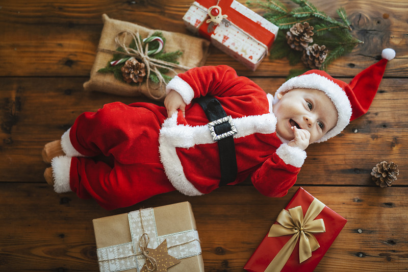 可爱的照片，穿着圣诞老人服装的婴儿躺在圣诞礼物中。摄影图片下载