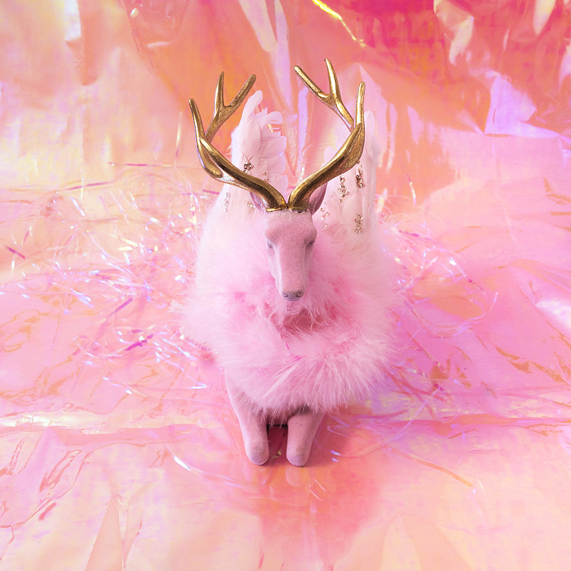 粉红色的驯鹿与粉红色的羽毛花环，粉红色的羽毛翅膀和金色的角在粉色的全息背景。超现实的幻想概念为圣诞节或尼年2023年问候卡片或横幅。图片下载