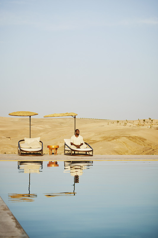 在沙漠营地，微笑的男子在泳池边的躺椅上放松图片下载