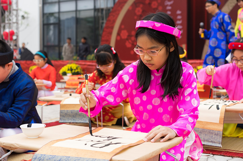 越南河内——2015年2月7日:在越南首都河内明开文中学举办的农历新年庆祝活动上，身着传统服饰的学生们正在学习书法图片下载