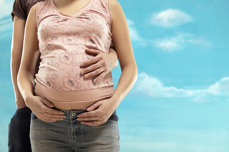 孕妇的中段和一个男人站在她身后，手放在她的肚子上图片素材