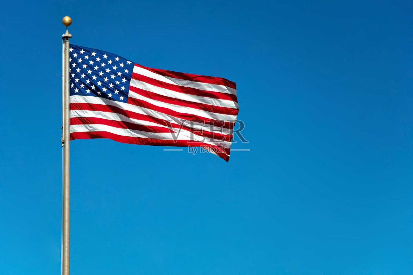 与之形成对比的照片是美国国旗在坚实的蓝天下飘扬照片摄影图片