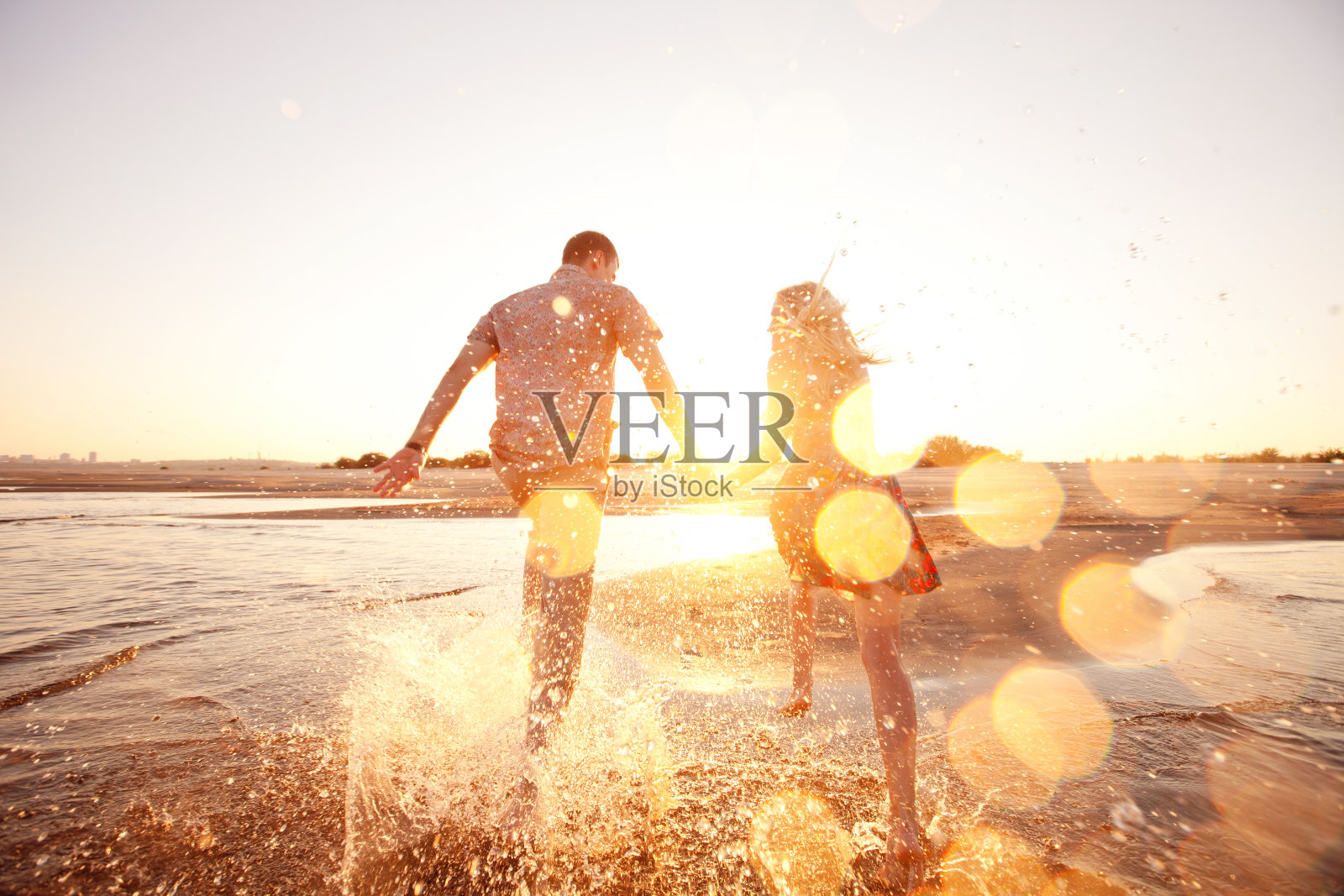 一对快乐的夫妇在阳光照耀的海滩上冲过海浪照片摄影图片