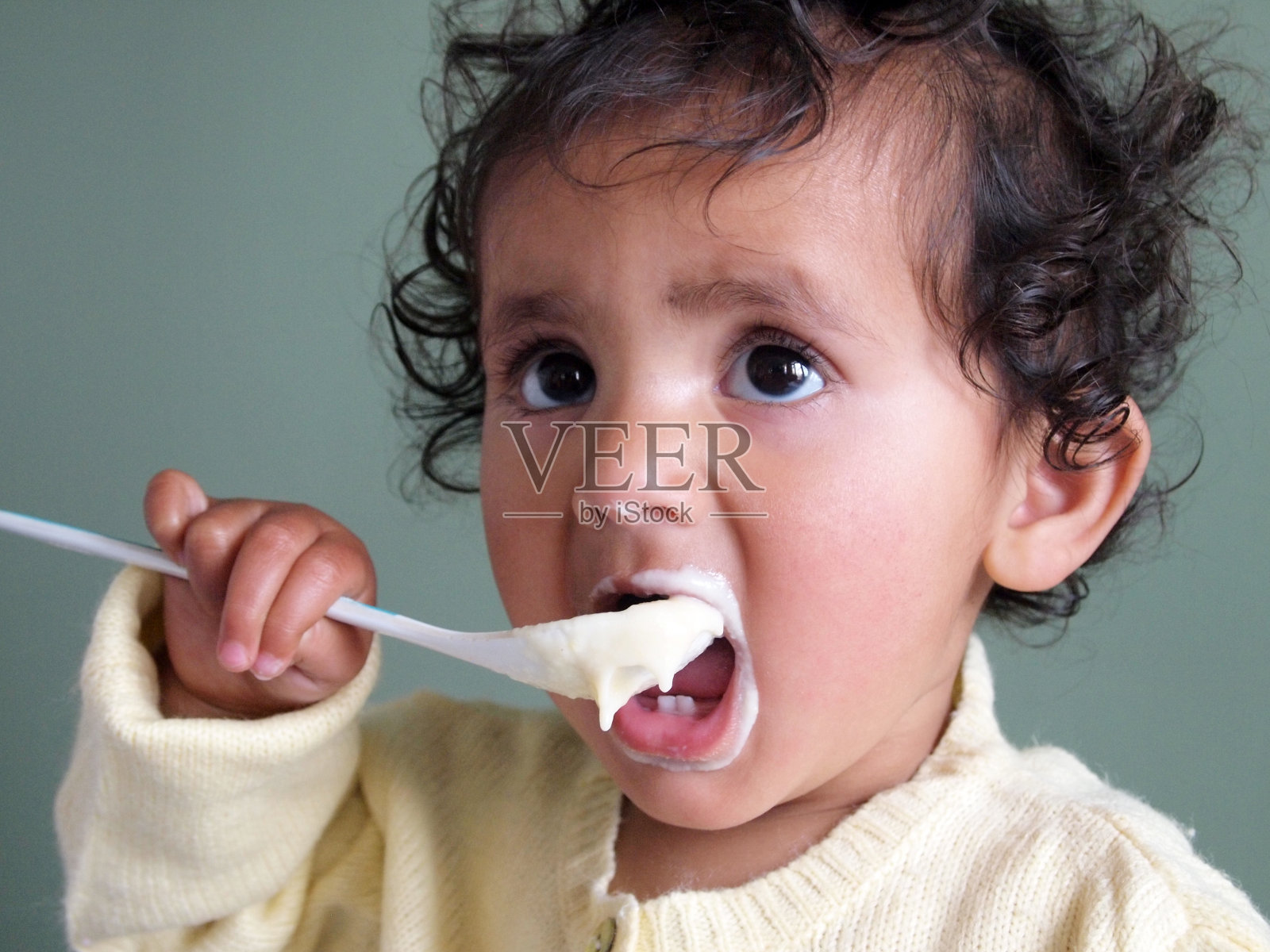 蹒跚学步的小女孩用一勺粥喂自己。照片摄影图片