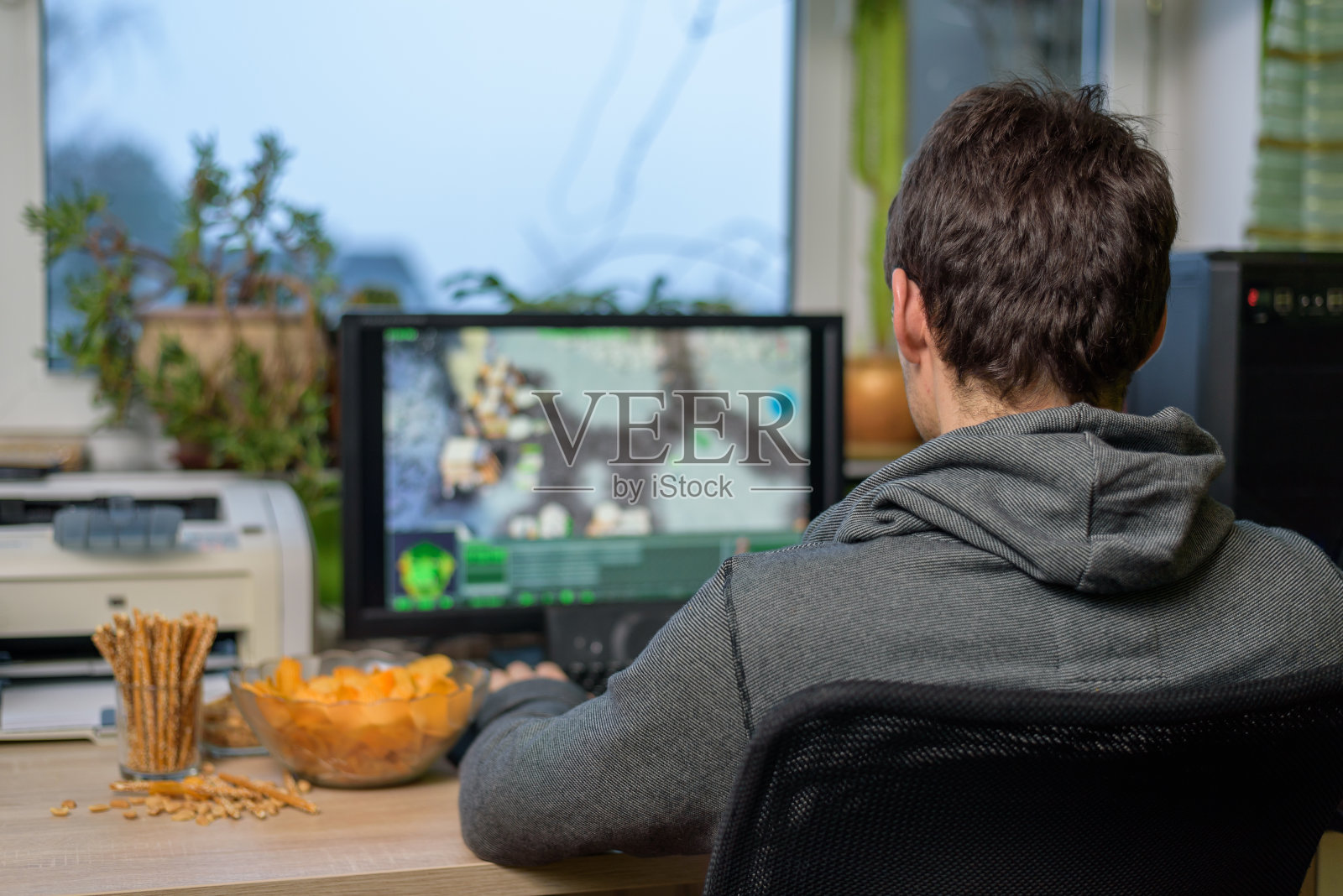 男性玩家在电脑上玩策略游戏吃零食照片摄影图片