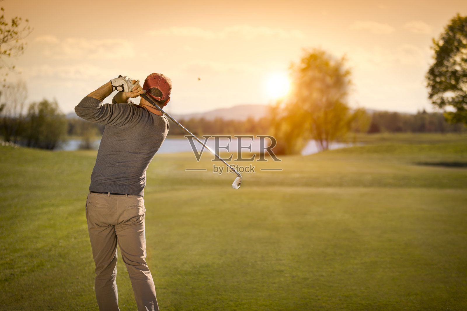 男性高尔夫球员在黄昏摆动高尔夫球杆。照片摄影图片