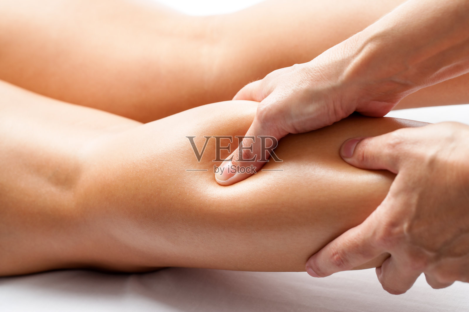 治疗师用拇指按压女性小腿肌肉。照片摄影图片
