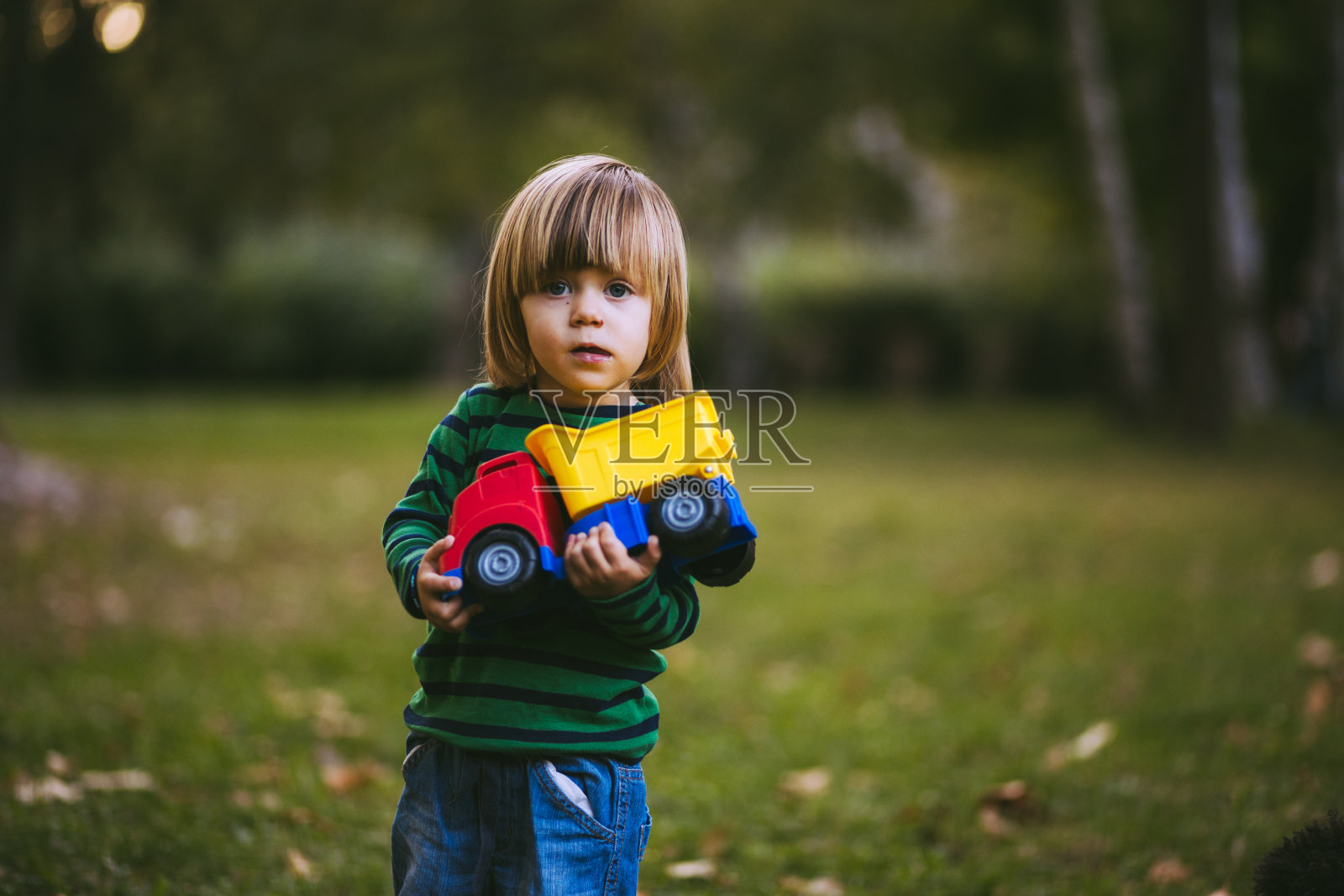 在公园里抱着玩具卡车的金发男孩照片摄影图片