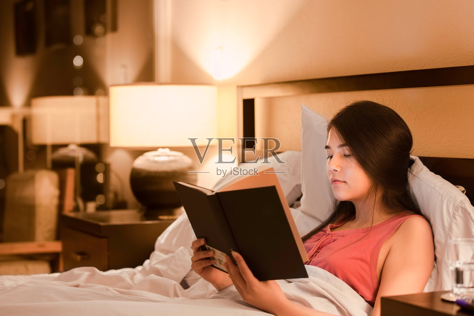 混血少女晚上在床上看书照片摄影图片